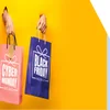 Hands popping out of a yellow backdrop holding Black Friday Cyber Monday branded shopping bags