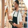 Male employee in an apron placing a bottle of alcohol on to a shelf