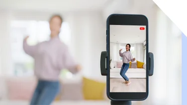 Photo of a woman behind a smartphone camera performing a TikTok dance trend
