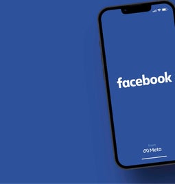 Phone with facebook logo on screen on a matching blue surface
