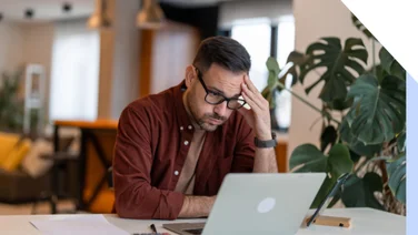 Man looking at his laptop screen with a frustrated look on his face and hand to his head