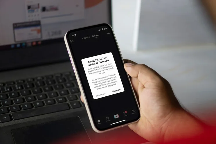A hand holding a smartphone with a ban message from TikTok on the screen