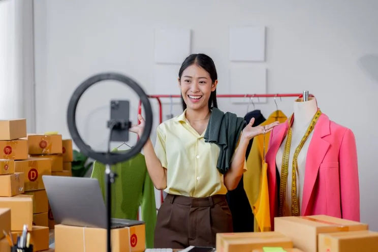 A woman in her clothes warehouse interacting with a camera in front of a ring light