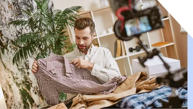 A man holding up a shirt in front of a camera on a tripod