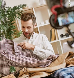 A man holding up a shirt in front of a camera on a tripod