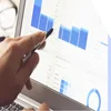 Photo of a hand with a pen pointing at graphs on a laptop screen