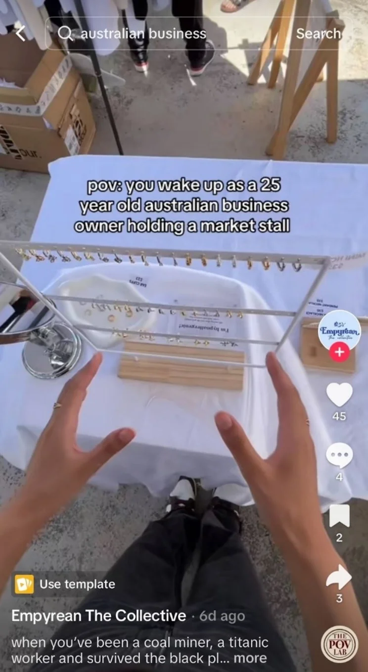Small business owner showing her market stall while holding her hands out with camera strapped to body