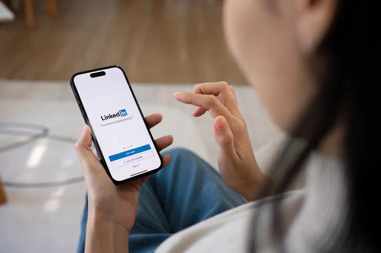 Woman holding a mobile phone with the LinkedIn login page on screen
