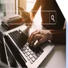 Hands typing on a keyboard while holding a phone with a search bar graphic on top