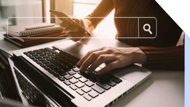 Hands typing on a keyboard while holding a phone with a search bar graphic on top