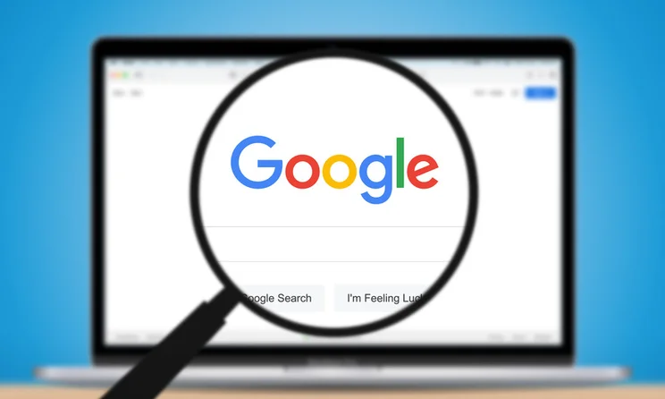 Magnifying glass hovering over a laptop screen showing the Google search homepage