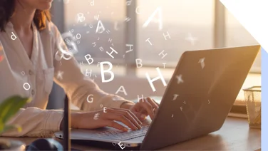 Woman typing at a laptop with floating letters around her hands