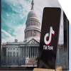 A phone with the TikTok logo on screen in front of a photo of the White House