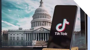 A phone with the TikTok logo on screen in front of a photo of the White House