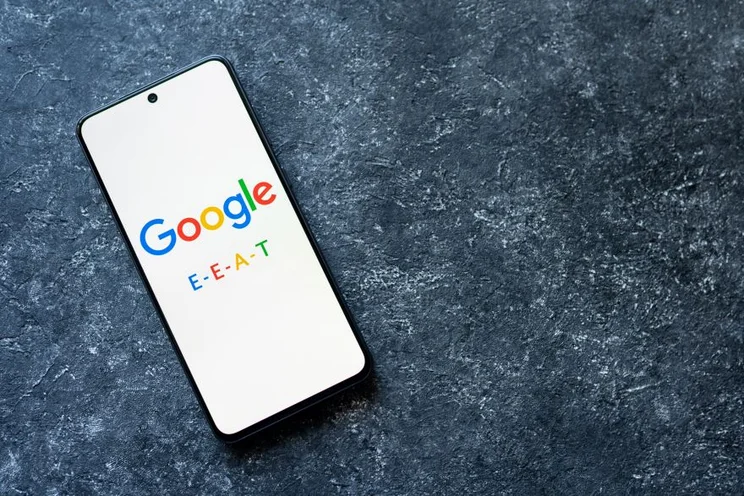 A phone with the google logo on the screen and text reading "E-E-A-T"