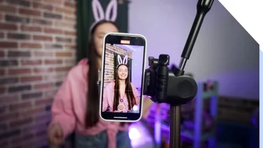 lady in bunny ears and a pink jumper filming herself with a smartphone held up with a tripod