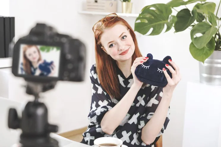 A smiling woman holding a bag in front of a video camera on record