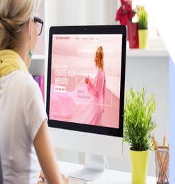 Woman sitting at desk looking at a desktop screen with a pink image of a woman on a beach