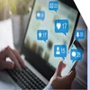 Hands typing on a laptop and holding a phone with social media interactions on screen