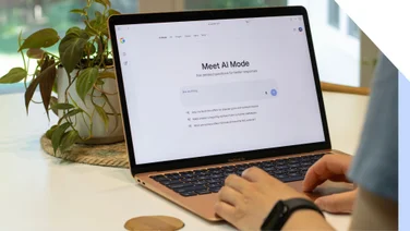 Hands typing on a laptop with the Google AI Mode landing page on screen