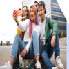 4 kids taking a selfie while sat on a skateboard in a parking lot