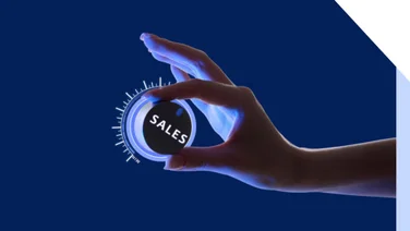 woman's hand cracking up a dial that says "Sales" on it