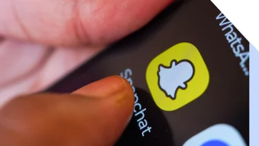 Close up image of a thumb tapping the snapchat logo on a smartphone homepage