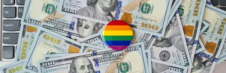 circular rainbow pin badge lying on a bed of scattered dollar notes