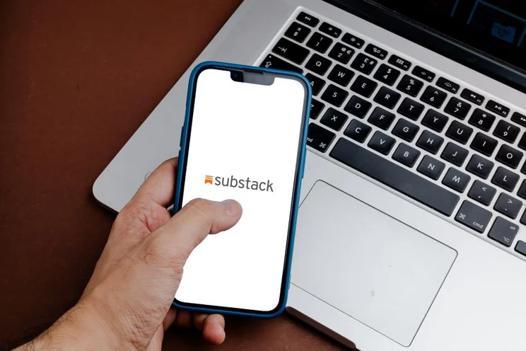 A hand using a smartphone with the Substack logo on screen