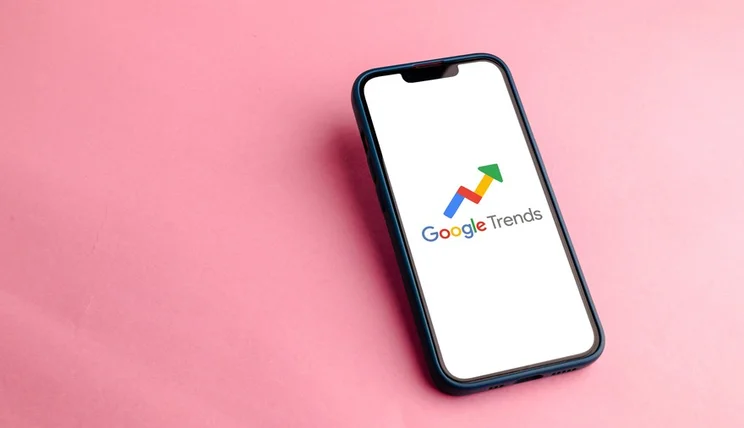 smartphone with the Google Trends logo on screen laying on a pink surface