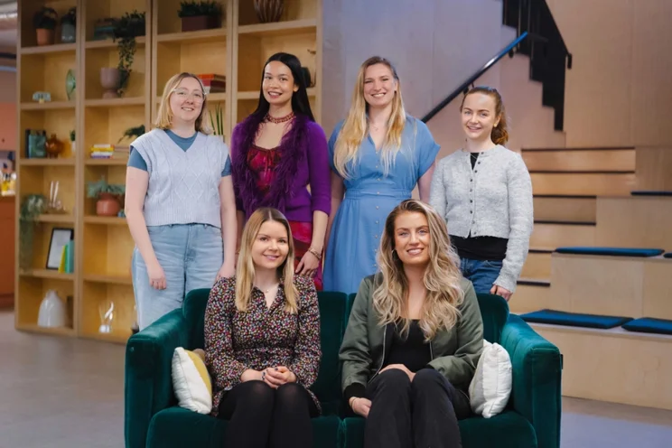 The six members of the WBE team sit and stand together, smiling at the camera