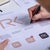 A designer sketches modifications on logo drafts featuring the initials