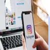 person scrolling on smartphone instagram app with the desktop instagram page open on a laptop