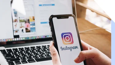 person scrolling on smartphone instagram app with the desktop instagram page open on a laptop