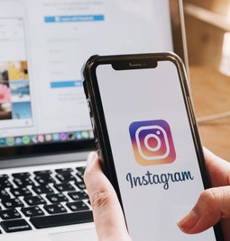 person scrolling on smartphone instagram app with the desktop instagram page open on a laptop