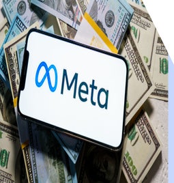 smartphone with meta logo on screen laying on top of a pile of cash
