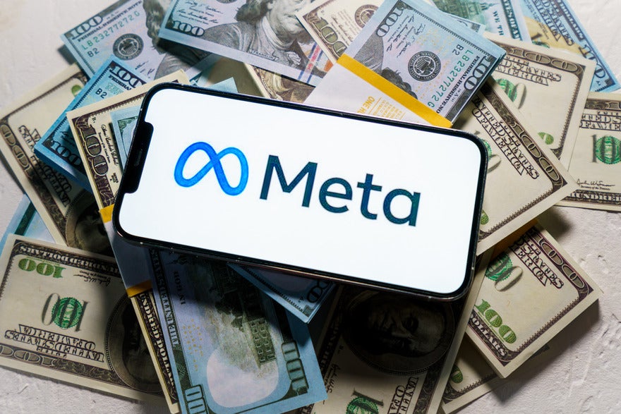 smartphone with meta logo on screen laying on top of a pile of cash