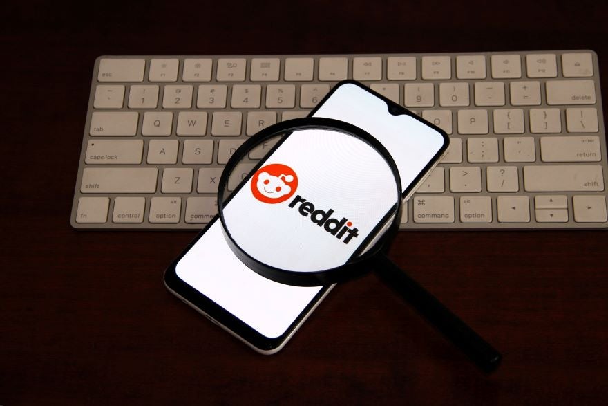 Reddit Phone Image A smartphone displaying the Reddit logo, viewed through a magnifying glass, resting on a keyboard.