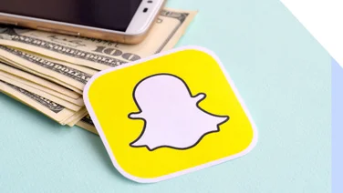 Sticker of snapchat logo laying on top of pile of dollar notes