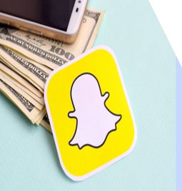 Sticker of snapchat logo laying on top of pile of dollar notes
