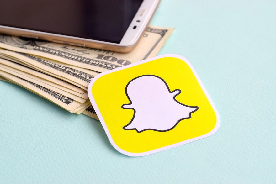 Snapchat Ad Spend Report Intro Sticker of snapchat logo laying on top of pile of dollar notes