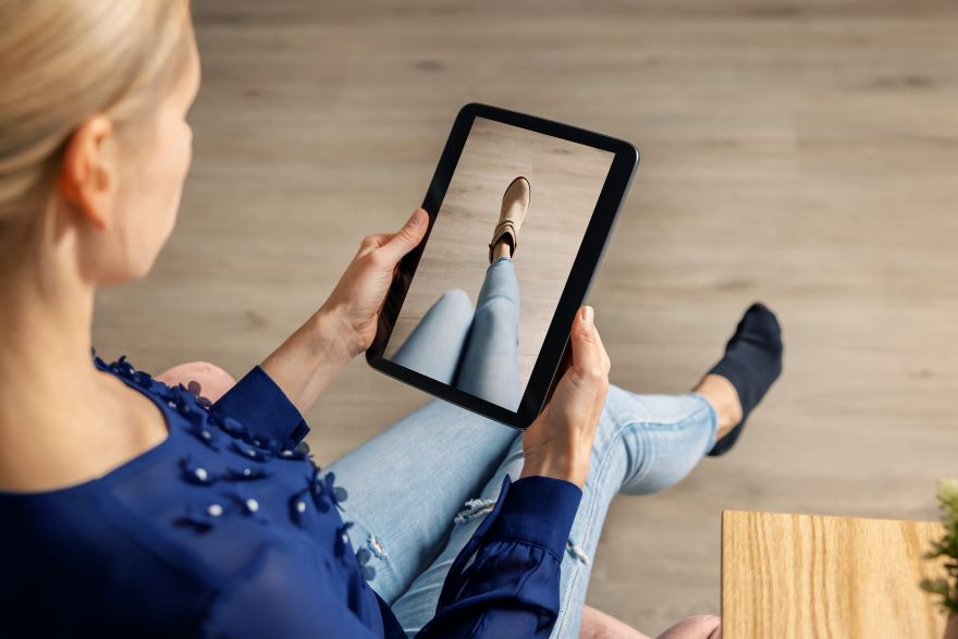 Virtual Clothes Try On A person holds a tablet displaying a close-up of a shoe worn with jeans, sitting in a cozy, modern setting.