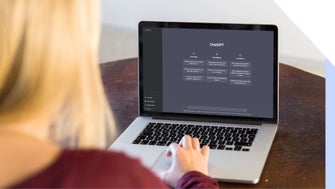 A person with long blonde hair sits at a wooden table, using a laptop displaying the ChatGPT interface with features and limitations.