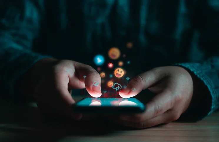 person typing on phone with emojis popping out the screen