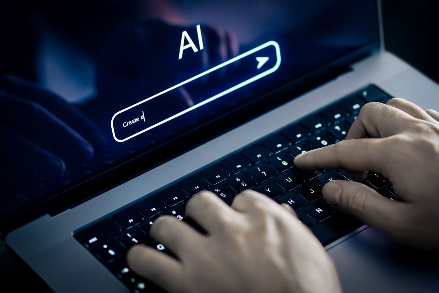 A person types on a laptop keyboard with a dark screen displaying "AI" and a search bar, suggesting an interaction with artificial intelligence.