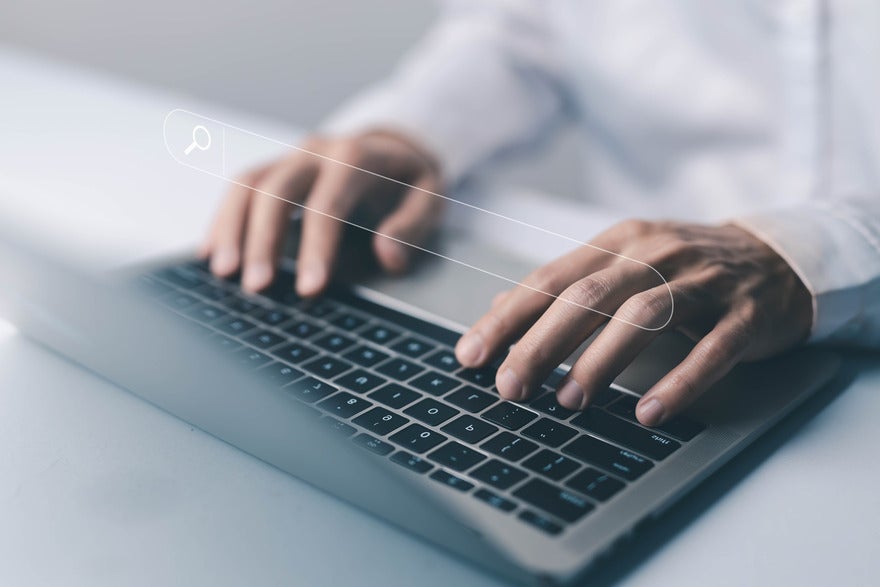 Hands typing at a laptop keyboard with a search bar image floating above