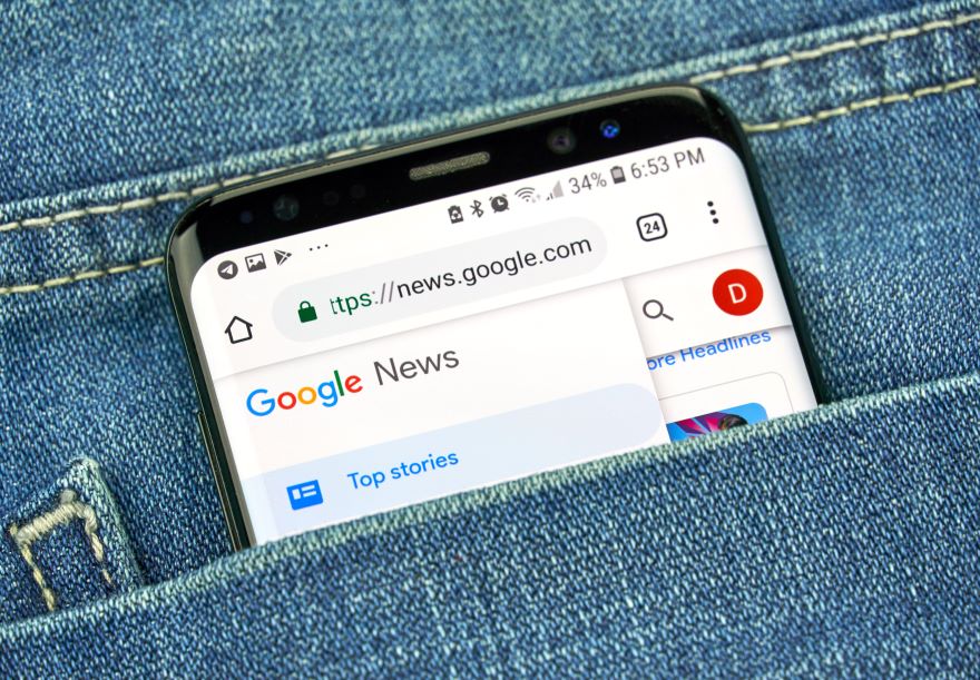 A smartphone displaying Google News peeks out of a denim pocket, showcasing the headlines on its screen.