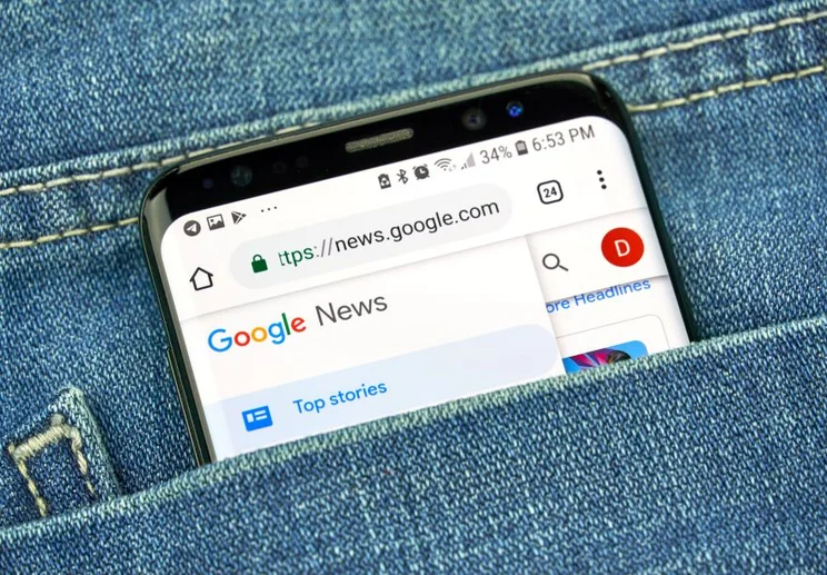 A smartphone displaying Google News peeks out of a denim pocket, showcasing the headlines on its screen.