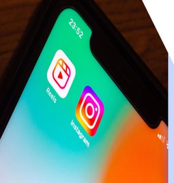 Close-up of a smartphone screen displaying the Instagram and Reels app icons against a gradient background
