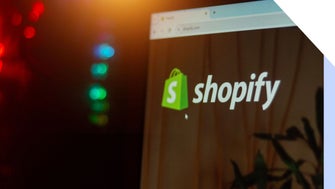 Close-up of a computer screen displaying the Shopify website logo with colorful lights in the background, hinting at a tech environment.
